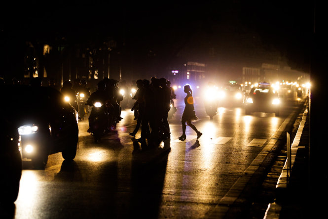 Người đân lợi dụng ánh đèn đường của ô tô xe máy lưu thông để di chuyển qua đường - Ảnh Nguyễn Khánh