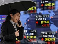A pedestrian uses her mobile phone before a share prices board in Tokyo, March 2012. Asian markets were mixed in cautious trade as dealers awaited key policy meetings at the central banks of the United States and Japan this week