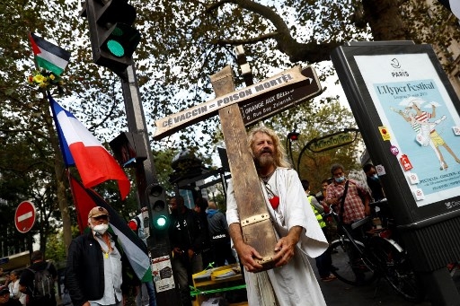 A man dressed as Jesus holds a cross and a sign reading 'Vaccine = lethal poison' during a rally against the compulsory Covid-19 vaccination for certain workers and the mandatory use of the health pass, near place du Colonel Fabien in Paris on August 28, 2021. Sameer Al-DOUMY / AFP